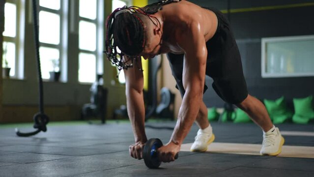 A man with gymnastic roller in his hands performs an exercise to strengthening the abdominal muscles. Training in a modern gym
