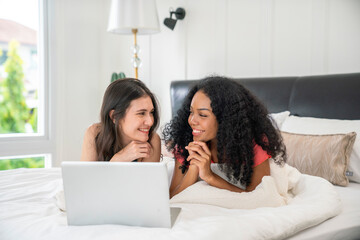 Happy lesbian couple having and using laptop in bedroom