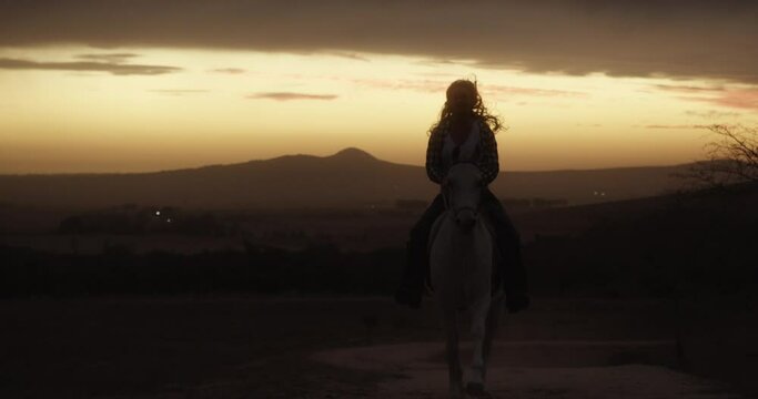 Woman, cowgirl and horse ride at sunset in countryside for travel or transport in nature. Female person or farmer riding on animal for outdoor adventure, journey or trip with silhouette at night