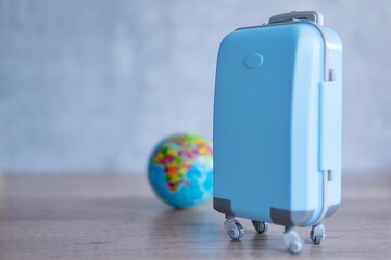 A blue luggage on a wooden table next to a globe. Copy space for text. Travel and vacation concept.