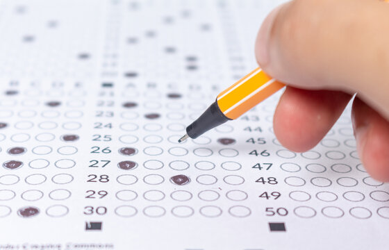 Hand filling out an exam answer sheet with a pen, concept for public and entrance exams.