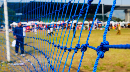 Close-up view of a rope net used as a goal net on a soccer field. Background of a football field in...
