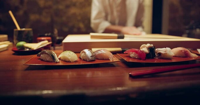 Chef, hands and sushi on plate, table and cleaning with cloth for presentation with fish, food and knife in restaurant. Person, server and cooking for protein, nutrition and meal in diner in Tokyo