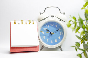 Desk calendar and blue vinatge clock on white background and green leaves as foreground stock photo