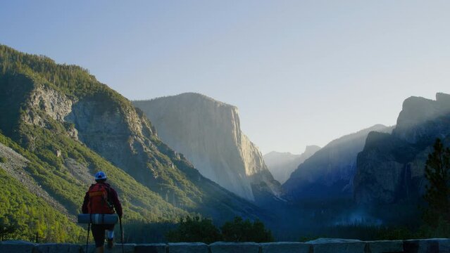 A hiker with raised arms stands in triumph against a stunning sunrise over a majestic mountain landscape. In Yosemite Park, Tunnel view, Camera 4K RAW. 