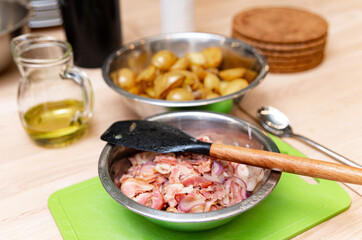 Cooked Potatoes and Bacon on Kitchen Counter. Roasted potatoes in a metal bowl and raw bacon strips...