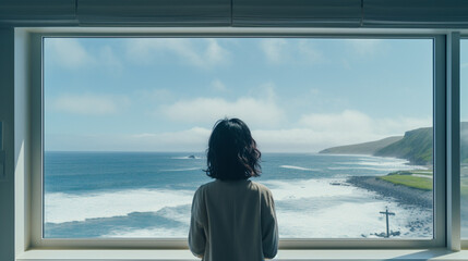 大きな窓から海を眺める女性の後ろ姿
