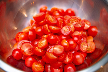 Sliced Cherry Tomatoes in Stainless Steel Bowl. Freshly cut cherry tomatoes in a reflective metal bowl, highlighting bright red colors and healthy ingredients for cooking.