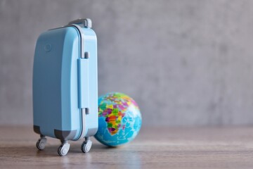 A blue luggage on a wooden table next to a globe. Copy space for text. Travel and vacation concept.