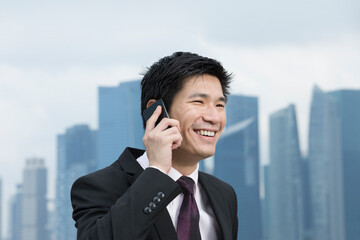 Happy Chinese business man talking on the phone in front of cityscape