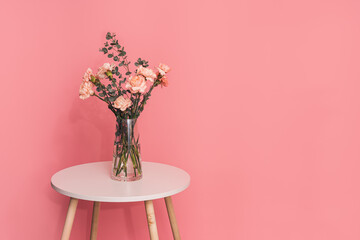 Bouquet of carnations with a eucalyptus branch in a glass vase on a round table against a pink...