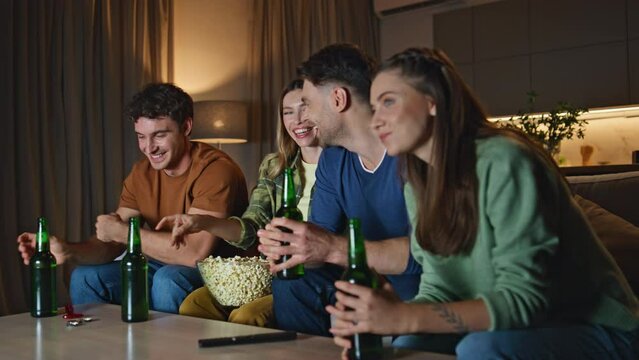 Cheerful friends watching television at night apartment. People drinking beer