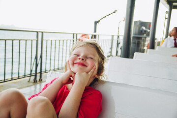 Cute little girl is sitting on the bench. A child is making funny faces. Children's emotions