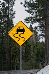Slippery when wet road sign with forest backdrop.  Vertical.  