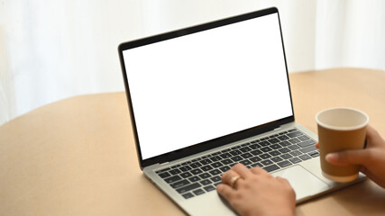 Fototapeta premium Businesswoman holding paper cup and working with laptop. Closeup view.