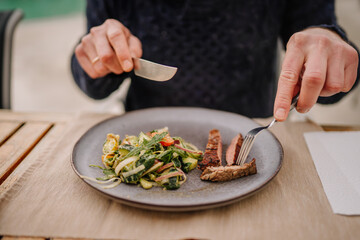 Sotogrante, Spain - January 25, 2024 - a close-up of hands cutting a steak with salad on a plate, on a wooden table.