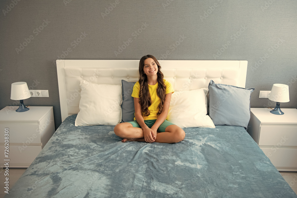 Wall mural Teenager child girl resting in bed at home bedroom. Kid relaxing in bedroom interior.