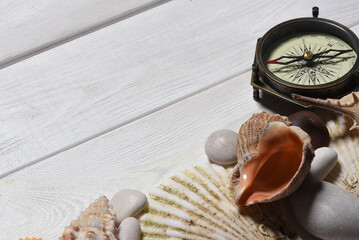 Vintage compass, seashells and pebble stones on the white wooden desk table close up background...
