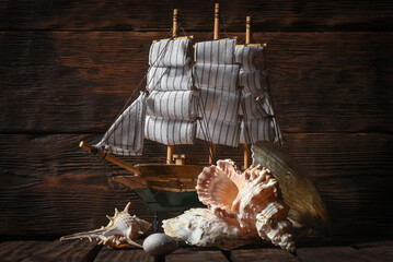 Sea travel concept background. Sea ship boat and seashells on the wooden desk table close up front...