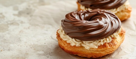 Two pastries with creamy filling and chocolate frosting on a light-colored surface.