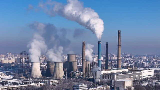 Rotating Drone View Of A Coal Power Plant Releasing White Smoke In The Atmosphere With A City In The Background, Europe