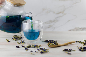 Blue anchan tea is poured from a glass teapot on a light background. Herb tea. Clitoria trifoliate
