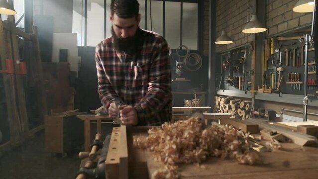 Carpenter planing wood in moody workshop