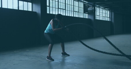 Image of shining light floating over woman exercising with ropes in an abandoned building