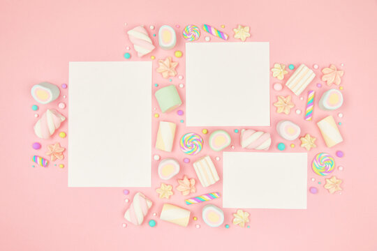 Set of three blank white cards on cute pastel pink kawaii background with frame of sweet candies, meringue and marshmallows . Flat lay, top view, copy space. Beautiful childlike design template