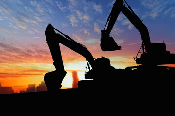 Two Crawler excavators silhouette are digging the soil in the construction site. on the sunset ...