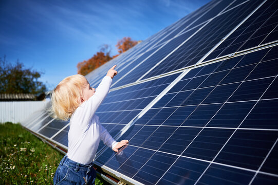 Little child looking at big solar panels. Interested boy investigates how does solar battery work. Small kid pointing at new panel. Concept of children and investment in renewable energy.