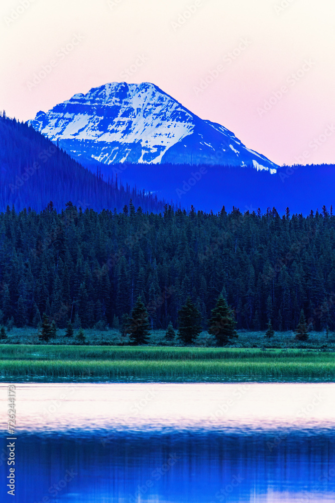 Wall mural Dusk by a lake in the forest with a mountain peak