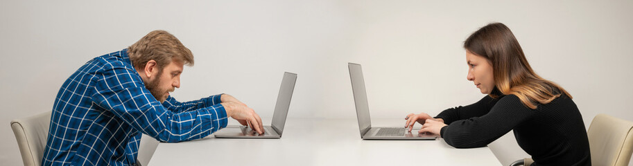 Young woman and emotional man in slouching position sitting in office room, working with laptop