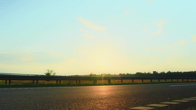 Delivery box cube van and white hatchback car are driving on highway at sunset countryside, out of town. Export import by light truck, logistic company. Traffic barrier guard rail. Speed