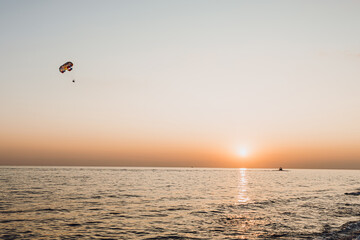 Parasailing.An active type of recreation at sea. A parachute floats in the sky. Vacationers rise above the water on a water parachute