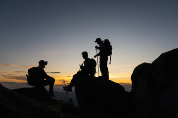 Silhouette group of mountaineers sitting on the rock at top of mountain, hiker group reaching summit