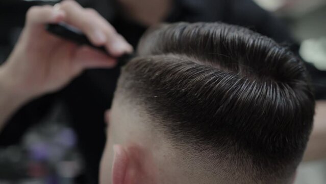 Beautiful haircut and hair styling in a barbershop. Combing hair with a comb after cutting, close-up. Slow motion