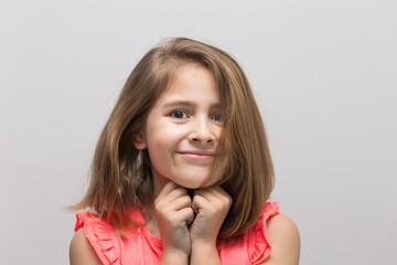 Little 8 years old with cheerful and smiling, with light brown hair and salmon color t-shirt with hands together under chin on white background. Concept of children and childhood