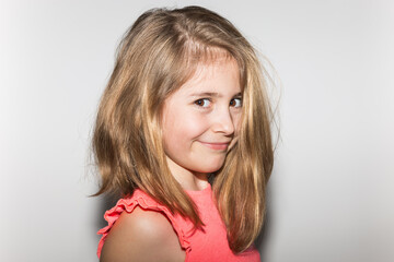 Portrait of a pretty 8 year old little girl in profile smiling and happy with light hair, salmon colored t-shirt and looking at camera on white background. Children and childhood concept