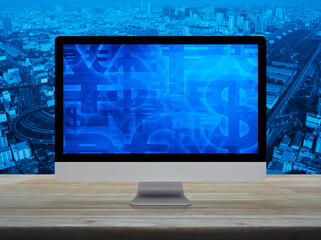 Financial currency symbol on desktop computer monitor screen on wooden table over city tower, street, expressway and skyscraper
