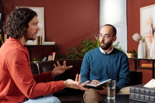 Selective focus shot of professional psychologist listening to his patient and taking notes at therapy session