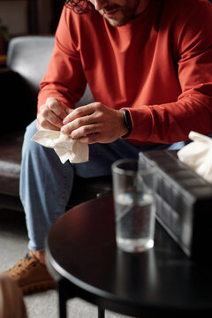 Vertical selective focus shot of young man suffering major depressive disorder fumbling tissue while having psychotherapy session