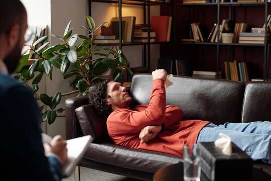Caucasian man lying on couch telling professional psychologist his troubles during therapy session