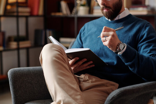 Selective focus medium section of bearded psychotherapist sitting on chair planning treatment and taking notes