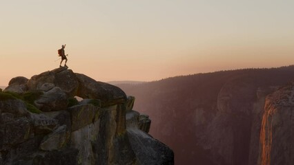The silhouette of an ecstatic hiker stands on a rocky mountain edge, arms outstretched, embracing the vastness at dusk. Yosemite national park. Slow Motion, Camera 4K RAW. 