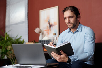 Medium portrait of Middle Eastern psychologist sitting in front of laptop taking notes while giving online consultation