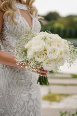 The bouquet with white flowers, roses, gypsophila and decorative plants on ceremony. Bride in an elegant dress holds a vintage bouquet. Wedding day. Beautiful bride portrait outdoors. Closeup.