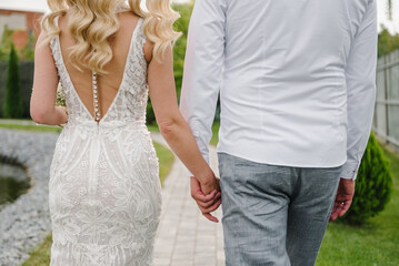 Bride and groom hold hands and walking on the street. Closeup. Details of wedding moments. Newlyweds together. Bride and groom walk outdoors. Back down view. Couple hands.