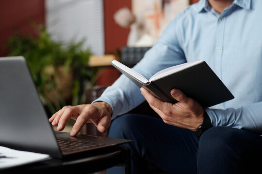 Unrecognizable man holding notebook searching information in Internet on laptop