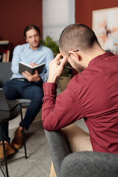 Selective focus rear view of unrecognizable sad man sitting on chair in front of psychologist having therapy session